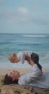 Portrait of Woman Lying on Sand with Ocean in Background and Holding Her Baby, Stock Footage