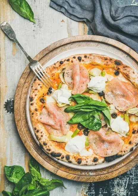 Freshly baked pizza with ham, artichokes, cheese and basil Photo